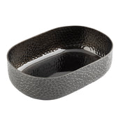 An aluminum oval bowl with a textured, mosaic-like exterior and a hammered, shiny black powder coat finish inside. This modern TableCraft bowl features slightly high sides and is photographed empty against a white background.