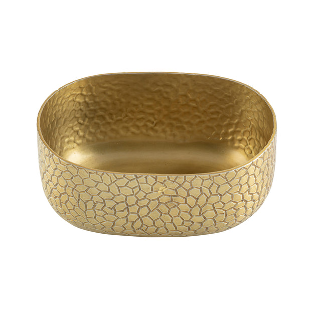 A shallow, oval-shaped aluminum bowl with a textured, hammered surface forming a pebble-like pattern. Smooth rounded edges and a gold powder coat finish softly reflect light across its detailed surface.