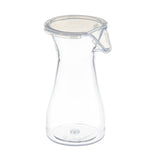 A clear, empty glass carafe with a wide base, narrow neck, and a transparent polycarbonate lid secured by a metal latch is shown standing upright on a white background.
