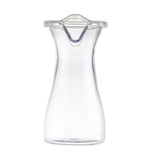 A clear, empty polycarbonate carafe with a curved body and wide base tapers towards the top. The top features a narrow spout and a transparent, slightly domed polypropylene lid with a small tab for easy removal. Photographed on a white background.