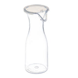 A clear, empty 19 oz polycarbonate carafe with a wide base and narrow neck. It features a transparent, round plastic lid secured by a metal clasp. The carafe stands upright on a white background, with no liquid or decoration inside.