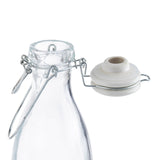 A clear glass carafe with a metal wire swing-top closure. The white ceramic cap with a rubber seal is open and attached to the carafe’s neck by the metal hinge. The background is plain white.