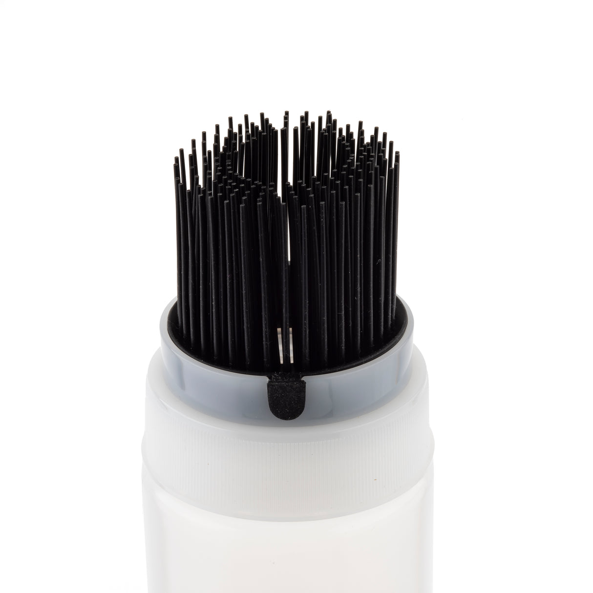 A close-up of a white cylindrical container with a gray rim, possibly an InvertaTop squeeze bottle, holding many black, thin, upright bristles grouped tightly at the top like a brush. The plain white background keeps the focus on the applicator.