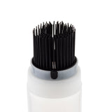 A close-up of a white cylindrical container with a gray rim, possibly an InvertaTop squeeze bottle, holding many black, thin, upright bristles grouped tightly at the top like a brush. The plain white background keeps the focus on the applicator.