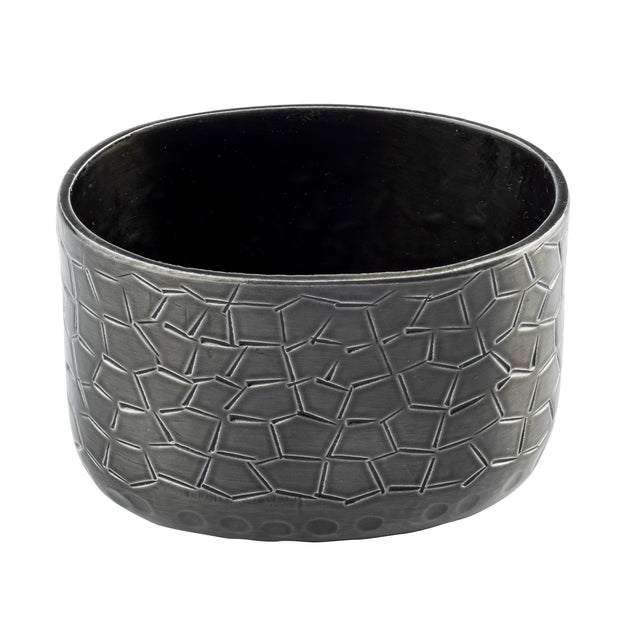 A round, black powder coated aluminum pot with a slightly oval shape. The exterior features a geometric, irregular polygon pattern in relief. The rim is smooth and the inside is unadorned, ideal as a modern sugar packet holder. Background is plain white.
