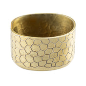 A wide, gold powder coated aluminum cuff bracelet with a matte finish and a geometric, honeycomb pattern etched onto its surface. The inside is smooth, while the exterior showcases a striking repeating polygonal design.