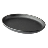 A TableCraft Cast Iron Sizzle Platter, black and oval-shaped with a slightly raised edge, is shown at an angle against a white background. Its matte, textured surface embodies the classic look of quality cast iron cookware.