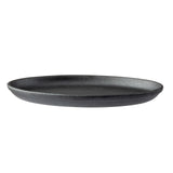 A black, round TableCraft sizzle platter with a matte, textured finish is shown against a white background. The plate has gently curved sides and a flat base, offering a minimalist, modern cast iron-inspired appearance.