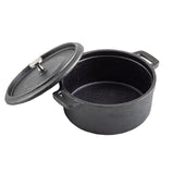 A black TableCraft cast iron Dutch oven with a textured surface is shown with its lid partially removed. The pot has two side handles and a metal knob on the lid. The Dutch oven rests on a white background.