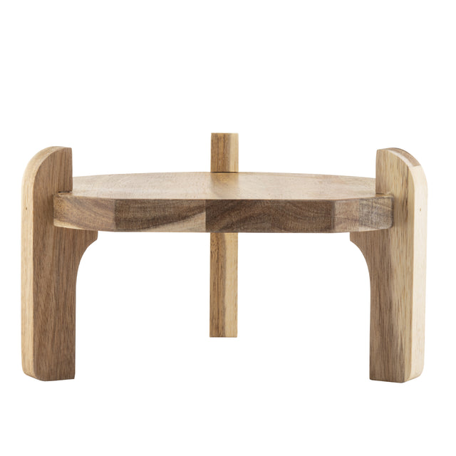 A small, round TableCraft beverage dispenser stand with three thick, curved legs and a smooth, flat top. Crafted from acacia wood with a natural finish and visible grain patterns, its minimalist and rustic design stands out against a plain white background.