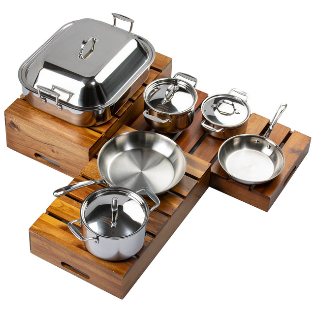 A Signature Cookware Set of five pieces with a sleek stainless steel finish, including pots, pans, and lids, displayed on wooden slatted trays. Features a large covered roasting pan, two saucepans, frying pan, and sauté pan—all with metal handles.