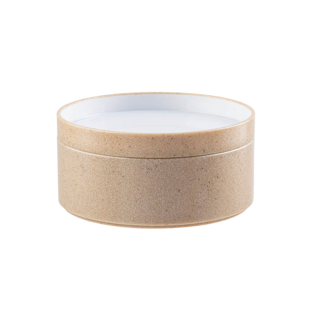 A round, beige, textured container with a removable lid, resembling natural cork. Crafted from styrene plastic, its inside is smooth and white, providing a clean contrast to the earthy exterior. The background is plain white.