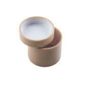 A small, round beige container with a matching lid, slightly tilted and resting on the edge of the open container. The simple, modern design is highlighted by a plain white background. This stackable piece is perfect for organized storage.