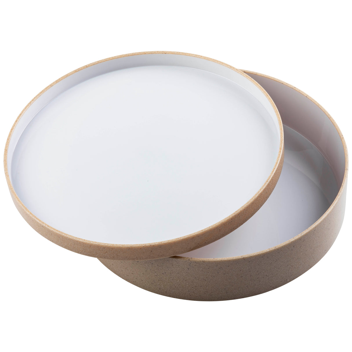 A round, shallow beige bowl with a white interior is shown with its matching lid slightly askew, revealing the inside. The stackable bowl and lid have smooth edges and a minimalist design, photographed against a plain white background.