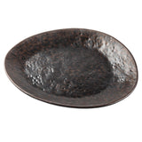 A dark, round ceramic plate with an uneven, slightly dimpled surface and a rustic brown speckled stone pattern, photographed against a white background. The plate features an irregular, organic shape and a matte finish.
