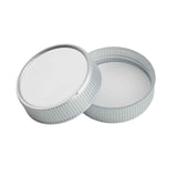 Two round, silver-colored replacement lids are shown. One lid lies flat with the open side facing up, while the other leans against it, displaying its smooth white inner surface and grooved texture on the outer edge.