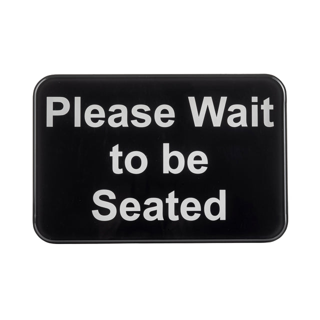 A rectangular black TableCraft 10901 self-adhesive sign with rounded corners displays the white text: “Please Wait to be Seated.” The message is centered, easy to read, and set against a plain background.