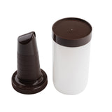 A white quart polyethylene container with a dark brown lid sits next to a matching, ridged Pourmaster Complete Unit nozzle attachment, both on a white background. The nozzle stands upright and separate from the container, which has its flat lid on top.