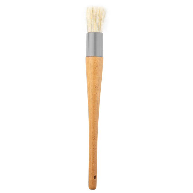 A basting brush with white boar hair bristles, a gray metal ferrule, and a smooth, light brown wooden handle featuring a small hole near the end for hanging, shown against a white background.