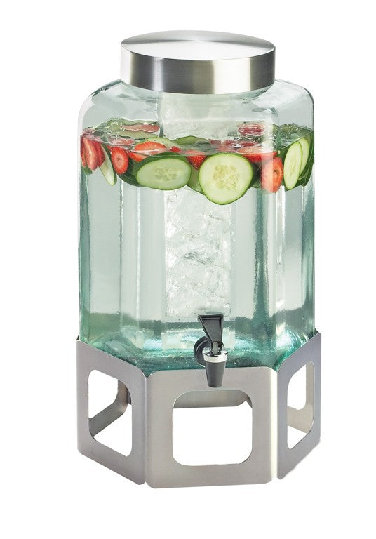 A 2 gallon beverage dispenser with a glass body is filled with water, ice, cucumbers, and strawberries. It features a metal lid, spigot at the bottom, and sits on a modern metal stand with square cut-out sides against a white background.