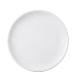 A plain white round plate from the Pulito Collection seen from above, featuring concentric ridges along the edge and a smooth, flat center. The background is white, highlighting the plate’s subtle texture and simple design.