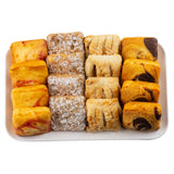 A rectangular white melamine serving platter holds fifteen assorted pastries in three rows: yellow sponge cakes with red swirls, powdered sugar-topped pastries, flaky golden pastries, and pastries with dark chocolate swirls, all neatly arranged.