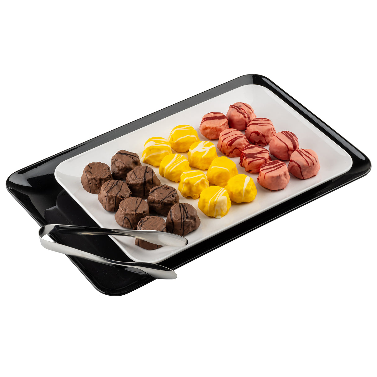 A rectangular white tray holds rows of bite-sized treats—brown, yellow, and pink, drizzled with icing. The tray sits on a black rectangular platter with metal tongs on the side. The background is plain white.