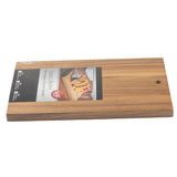 A rectangular wood board with a round hole in one corner. The product label shows tacos on an Acacia serving board and reads "Artisan Collection Reversible Acacia Chop Block." The board is photographed on a white background.