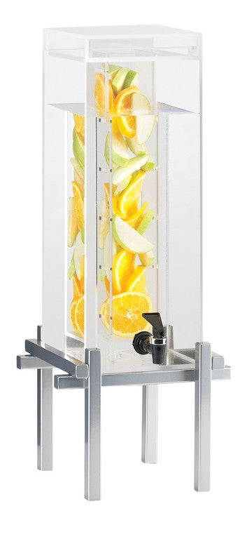A clear, tall 3-gallon beverage dispenser with an infusion chamber and a spout at the bottom sits on a silver metal stand. Inside, water is infused with slices of oranges, lemons, and green apples. The dispenser features a flat, transparent lid.