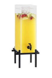 A tall, clear 5 gallon beverage dispenser filled with yellow juice, ice, and fruit slices sits on a black metal stand. It features a spigot near the base for easy serving, while apples and strawberries float inside for added flavor.