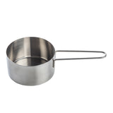 A stainless steel measuring cup with a straight-sided, brushed metal body and a long, thin, looped wire handle is shown on a white background. Dishwasher safe, the empty cup is positioned at an angle to display both the cup and handle.