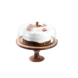 A chocolate cake with white frosting and strawberries on top sits on a TableCraft Products acacia cake plate, covered by a clear glass dome with a wooden knob handle, against a plain white background.