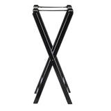 A black TableCraft tray stand with folding X-shaped legs and two parallel support straps across the top, designed to hold suitcases. The simple, minimalist structure is photographed against a white background.