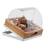 A wooden and metal display case with a clear, hinged half-size polycarbonate cover contains various pastries, including muffins and croissants. The lid is partially open, and the tray has built-in handles and supports for angled display.