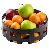 A round, black galvanized steel basket filled with assorted fruit, including green apples, red apples, and small orange tangerines, all arranged against a white background.