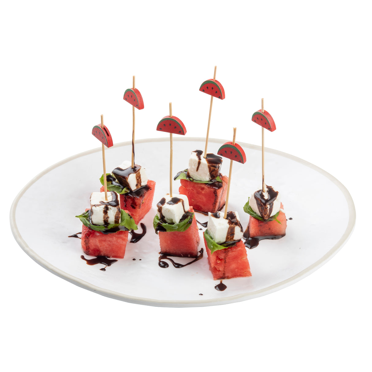Six appetizer skewers with watermelon cubes, basil leaves, and feta cheese topped with balsamic glaze are arranged on a white plate. Each skewer uses Natural Bamboo Decorative Picks by TableCraft with a small watermelon image at the top.