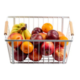 A powder coated steel storage basket with wooden handles holds apples, oranges, plums, peaches, and bananas. Filled with colorful fresh fruits, the basket is set against a white background.