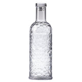 A clear, textured TableCraft carafe with a cylindrical body and narrow neck, filled with water. The 34 oz bottle features a faceted geometric pattern and is sealed with a transparent, flat-topped cap, standing upright on a plain white background.