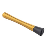 A gold muddler with a smooth, tapered handle and a black, textured flat end designed for crushing herbs or fruit. The stainless steel muddler is photographed on a white background, positioned diagonally from bottom right to top left.