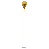 A long, gold bar spoon with a twisted, slender stem and a large, rounded, teardrop-shaped top stands vertically on a small circular base against a white background.