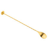 A Gold Bar Spoon with a twisted handle, a flat circular disc at one end, and an oval-shaped spoon at the other, is positioned diagonally on a white background.