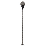 A long, thin stainless steel Bar Spoon with a twisted shaft stands upright on a small round base. The top features a large, teardrop-shaped paddle, blackened at the edges and fading to metallic grey. The background is plain white.