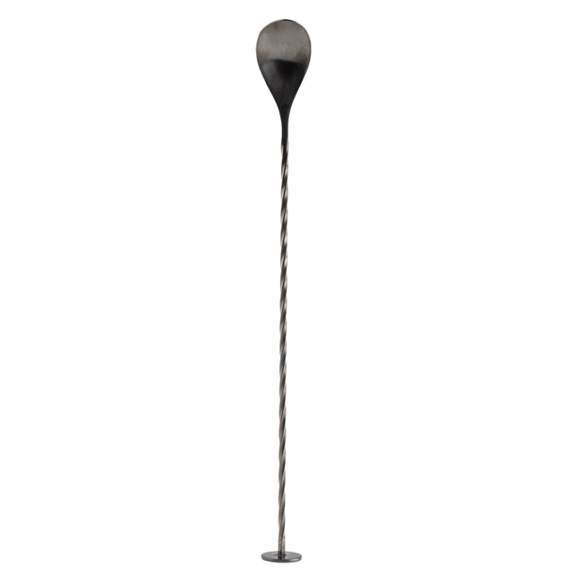 A long, thin stainless steel Bar Spoon with a twisted shaft stands upright on a small round base. The top features a large, teardrop-shaped paddle, blackened at the edges and fading to metallic grey. The background is plain white.
