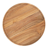 A round, light-brown TableCraft serving board crafted from acacia wood, featuring a slightly raised rim. Natural wood grain and color variations are visible. The board is photographed from above on a white background.