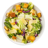 A white melamine serving bowl filled with Caesar salad, featuring crisp romaine lettuce, croutons, shaved parmesan cheese, and bits of purple cabbage. The fresh ingredients are colorful against a plain white background.