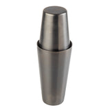 A stainless steel cocktail shaker with a sleek gunmetal finish stands upright. The top cap fits securely onto the larger base, creating a smooth, cylindrical silhouette. Its dark, matte surface is modern and free from any visible markings.