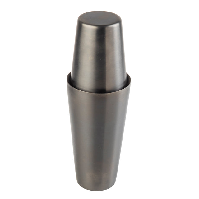A stainless steel cocktail shaker with a sleek gunmetal finish stands upright. The top cap fits securely onto the larger base, creating a smooth, cylindrical silhouette. Its dark, matte surface is modern and free from any visible markings.