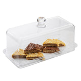 A clear rectangular cake dome sits atop a TableCraft cake plate, covering six triangular dessert bars with assorted chocolate and white toppings on a transparent tray. The dome features a round knob, while the bars are neatly arranged in two layers.