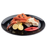 A black TableCraft Products melamine serving platter holds cooked crab legs, two halved lemons, and a red crab cracker, all neatly arranged against a plain white background.