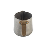 A small stainless steel frothing cup with a matte finish, featuring a wide spout and a sturdy, angular brass handle attached with two visible rivets. The minimalist, industrial pitcher is photographed on a white background.